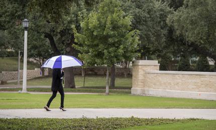 Pedestrian with umbrella walks across campus