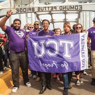  A group TCU students walks across the Edmund Pettus Bridge in Selma, Alabama. They hold a TCU flag and several students make the wo-fingered Go Frogs hand gesture.