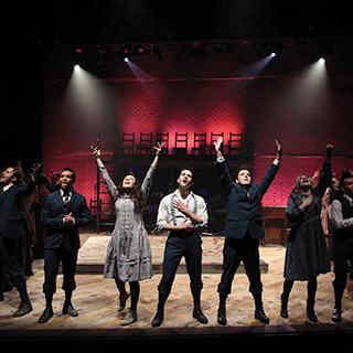 Student actors in a theatrical production of Spring Awakening sing together on stage